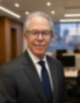 Man with glasses and mustache in a suit smiles in a modern office. Background shows desks, computers, and large windows.